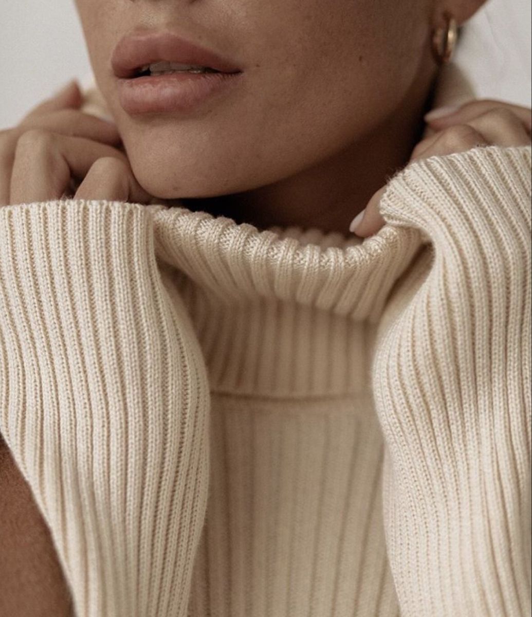 Close crop of a ribbed cream turtleneck held at the chin