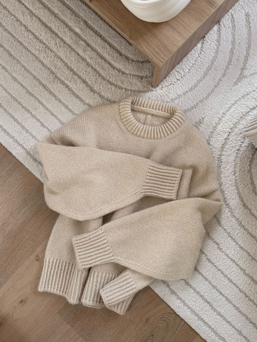Beige knit sweater laid on a patterned rug beside a wood table