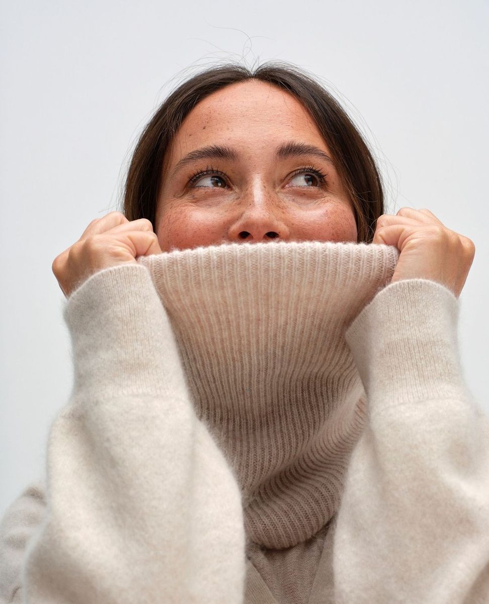 Smiling woman pulling a cream turtleneck up over her nose