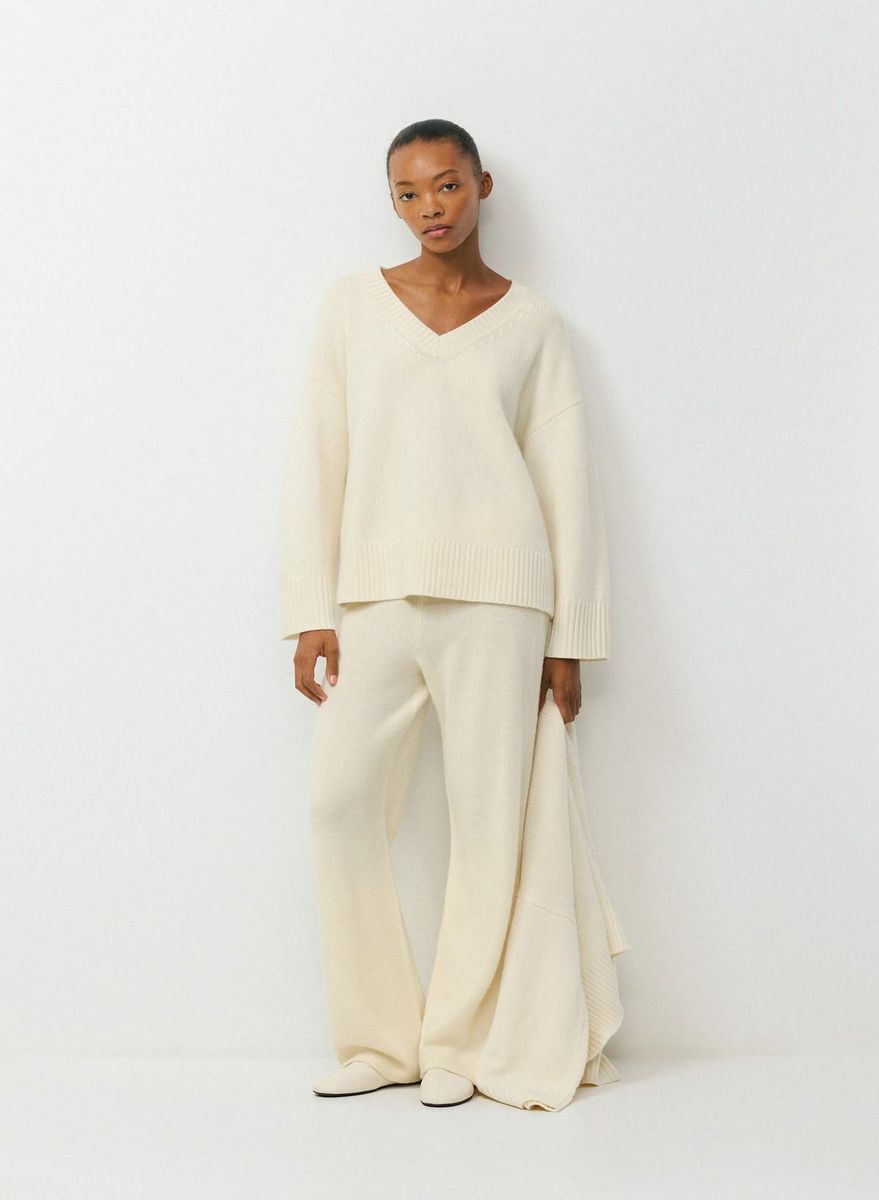 Woman in a cream knit set standing against a white wall