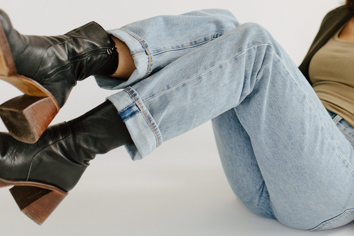 Legs in light denim and black leather boots raised against a white backdrop