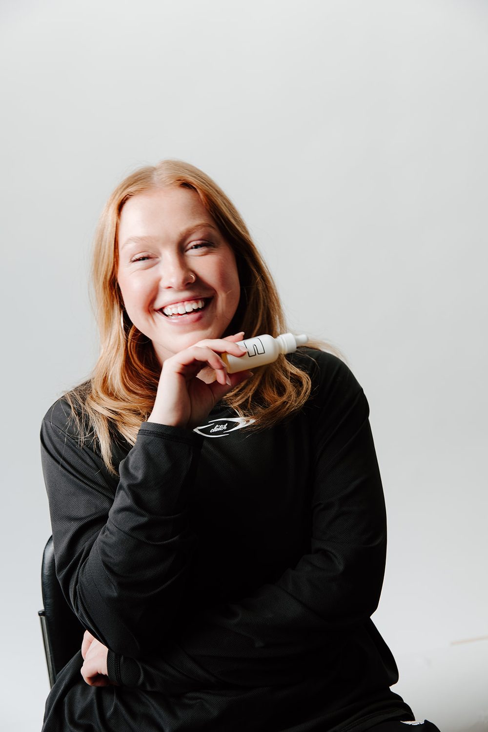 Woman laughing with a small white dropper bottle held at her chin