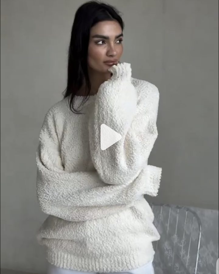 Woman in an oversized cream bouclé knit with her hand at her chin, looking off to the side