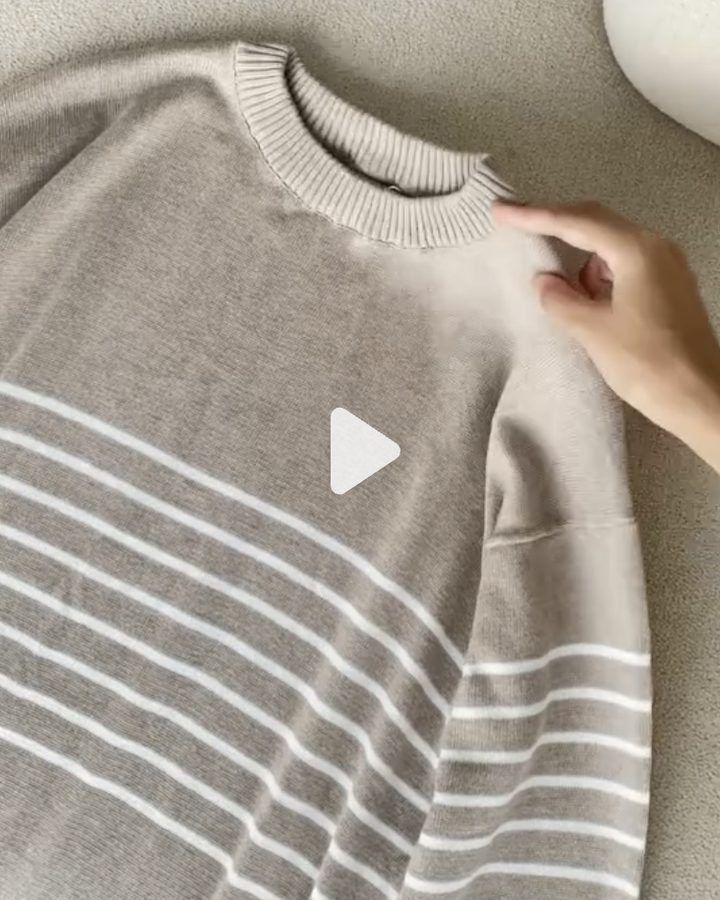Hand smoothing a taupe striped crew neck knit laid flat on a boucle sofa